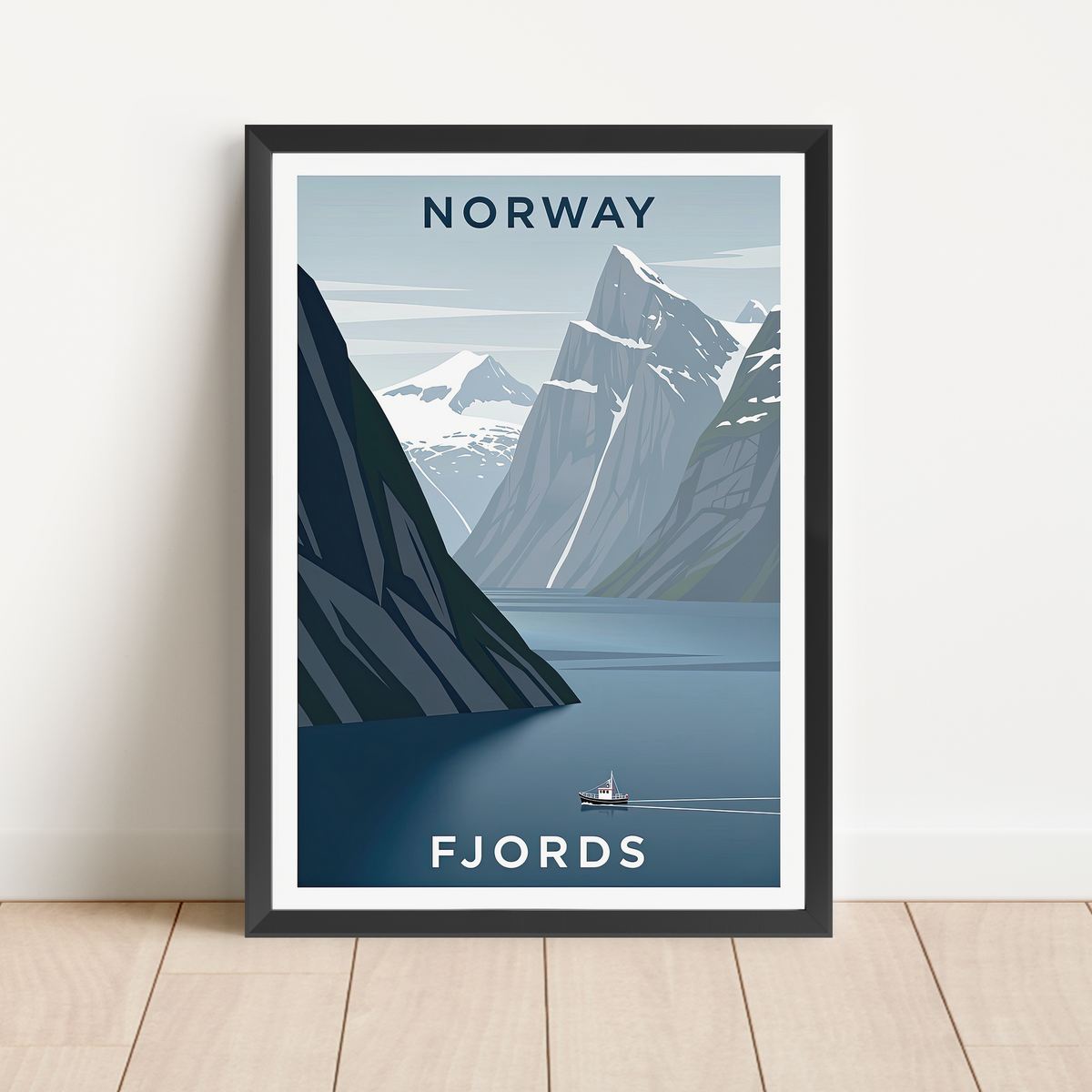 A framed travel poster of Norway's fjords, leaning against a white wall on a light wood floor. The poster features a stylized illustration of blue water, steep gray mountains, and snow-capped peaks, with the words 'NORWAY' at the top and 'FJORDS' at the bottom.